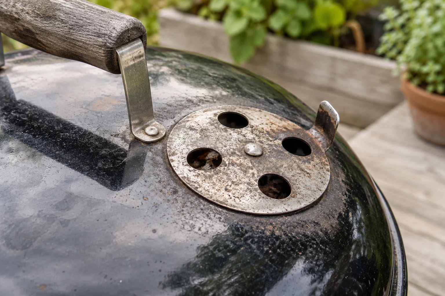 Close detail of a real circular metal top vent on a charcoal kettle lid, partially open holes and worn metal textures, no hands